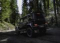 A black Mercedes-Benz G 63 SUV drives on a dirt path surrounded by tall, dense forest trees in daylight.