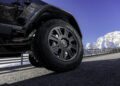 Close-up view of a BRABUS XLP 800 ADVENTURE tire and wheel on a black Mercedes-AMG G63, parked on a paved mountain road with snow-covered peaks and a blue sky in the background.