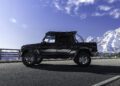 A Mercedes-AMG G63 off-road vehicle is parked on a paved road with snow-covered mountains and a partly cloudy blue sky in the background.