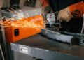A person at Bentley & Hedley Studios wearing protective gloves uses an angle grinder on metal, producing bright sparks in a workshop setting, showcasing the Production of the Blower Jnr.
