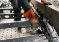 A person wearing protective gloves and orange sleeves uses clamps to secure metal parts on an industrial workbench at Hedley Studios.