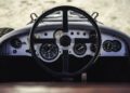 View of a classic car dashboard, featuring a large steering wheel and analog gauges, seen from the driver's perspective—a timeless design inspired by Bentley & Hedley Studios production Blower Jnr models.