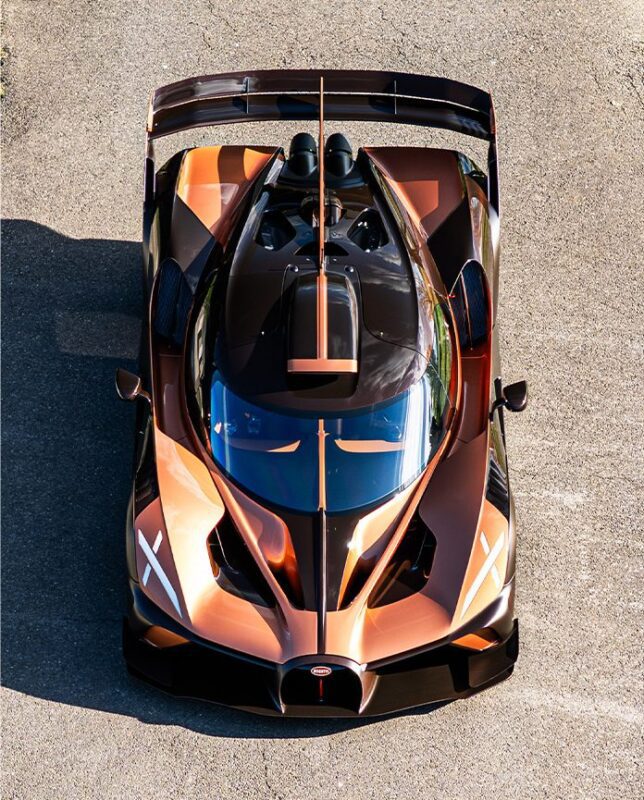 Aerial view of a bronze and black Bugatti Bolide supercar parked on a paved surface, featuring carbon fiber accents, a large rear wing, and aerodynamic design details.