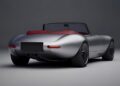 A silver convertible sports car with a red interior, inspired by FormerJaguar Designer Ian Callum Reimagines A Modern-Day E-Type, is parked in a studio setting, viewed from the rear and slightly to the side.