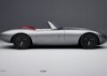 A silver convertible sports car with a sleek, minimalist design and red interior, viewed from the side against a plain gray background—Former Jaguar Designer Ian Callum reimagines a modern-day E-Type in stunning detail.