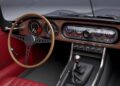 Classic car interior inspired by Former Jaguar Designer Ian Callum Reimagines A Modern-Day E-Type, featuring red leather seats, wooden steering wheel, analog gauges, modern digital display, manual gear shift, and wood dashboard.
