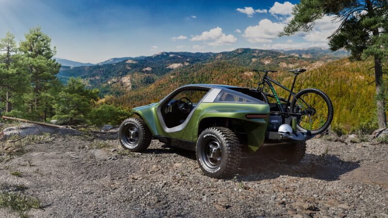 A green off-road vehicle with large tires is parked on a rocky area overlooking forested mountains, showcasing Expedition Elegance with a bike mounted on the rear.