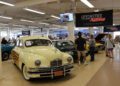 Vintage cars are displayed indoors at the 2025 Spring Carlisle Auction, with attendees walking and viewing the vehicles under banners and bright lighting.