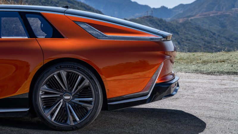 Rear view of an orange luxury car parked outdoors, showing the taillight, wheel, and part of the mountain landscape in the background.