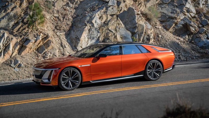 Orange luxury electric car parked on a mountain road with rocky terrain in the background.