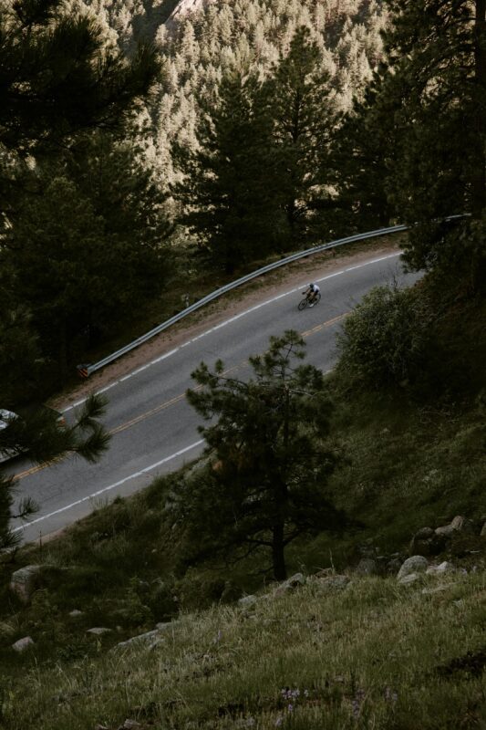 A person rides a bicycle uphill on a winding road surrounded by dense trees and greenery, exploring one of the scenic off-roading destinations perfect for nature enthusiasts.