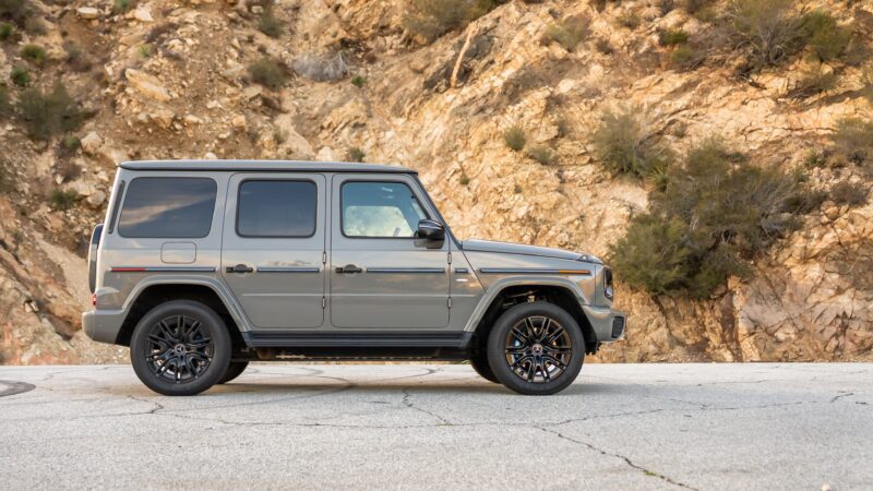 An electrified Mercedes G-Class SUV, an enduring icon, is parked on a paved surface with a rocky hillside in the background.