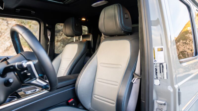 Close-up view of the front seats and interior of a modern Mercedes vehicle, with the driver’s side door open and dashboard partially visible, highlighting its electrified features.