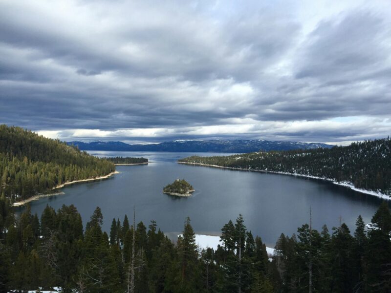 A lake surrounded by dense pine forests and mountains under a cloudy sky, with a small island in the center—one of the hidden gems among U.S. off-roading destinations.