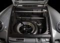 Open car front trunk showing a spare wheel secured with a strap, tools, and mechanical components neatly arranged inside a clean storage area—perfectly prepared for display at the Celebration Exotic Car Festival by Classic 9 Motorwerks.