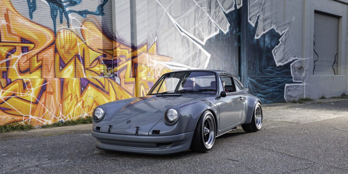 A gray classic sports car from Classic 9 Motorwerks is parked on a street in front of a building with colorful graffiti and a monochrome mural, evoking the vibrant energy of an exotic car festival.