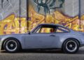 A silver classic sports car from Classic 9 Motorwerks is parked in front of a colorful graffiti-covered wall, ready to shine at the upcoming Celebration Exotic Car Festival.
