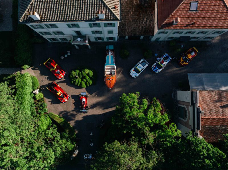 Aerial view of a courtyard at Cavallino Classic Modena 2025, displaying several sports cars and a boat, surrounded by buildings and greenery—an event known for record attendance and Best of Show winners.