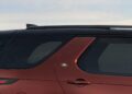 Side view of the rear section of a maroon SUV with tinted windows, a roof rail, and a visible Land Rover badge near the rear passenger door as Land Rover marks 35 years of Discovery with Gemini and Tempest Special Editions.