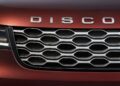 Close-up of the front grille of a red vehicle, featuring "DISCOVERY" in chrome letters above the hexagonal grille design—highlighting Land Rover Marks 35 Years Of Discovery With Gemini And Tempest Special Editions.