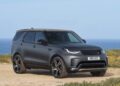 A black Land Rover Discovery SUV is parked on a dirt path with grass and the ocean in the background under a clear sky, as Land Rover marks 35 years of Discovery with Gemini and Tempest Special Editions.