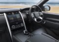 Interior view of a modern SUV, showing the dashboard, steering wheel, and infotainment screen—perfect for adventure, just as Land Rover marks 35 years of Discovery with Gemini and Tempest Special Editions. The beach and ocean shine outside the windows.