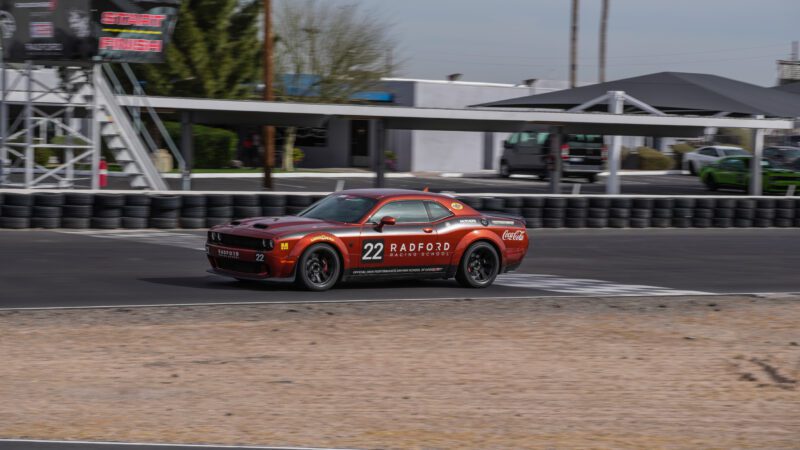A red Dodge sports car with the number 22 and Radford Racing School branding drives on a racetrack near a start/finish line.