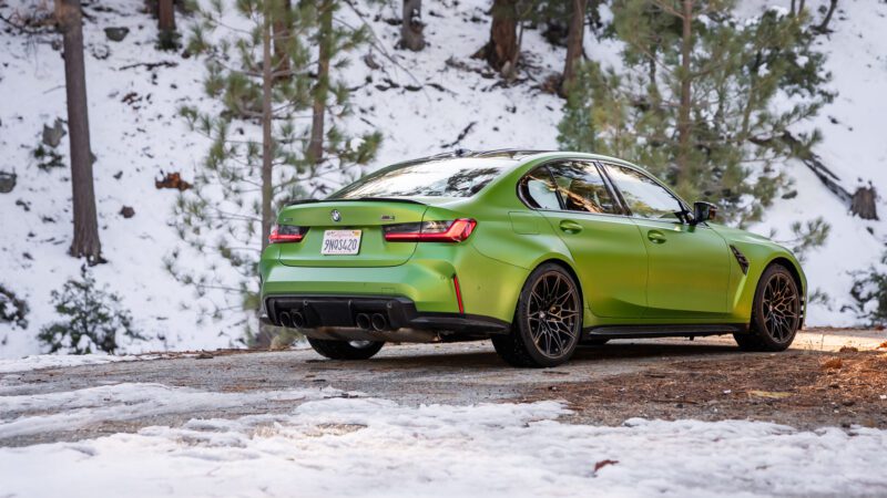 A green BMW sedan parked on a snowy, wooded road with pine trees in the background.