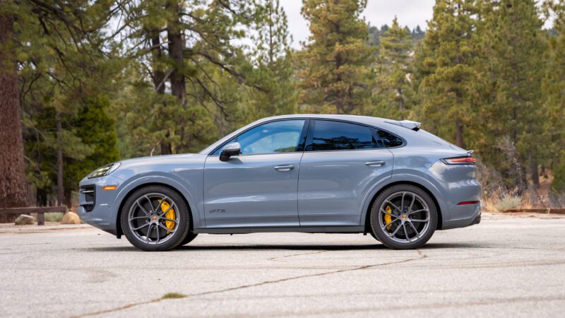 A gray Porsche Cayenne GTS parked on a paved area with trees and greenery in the background.