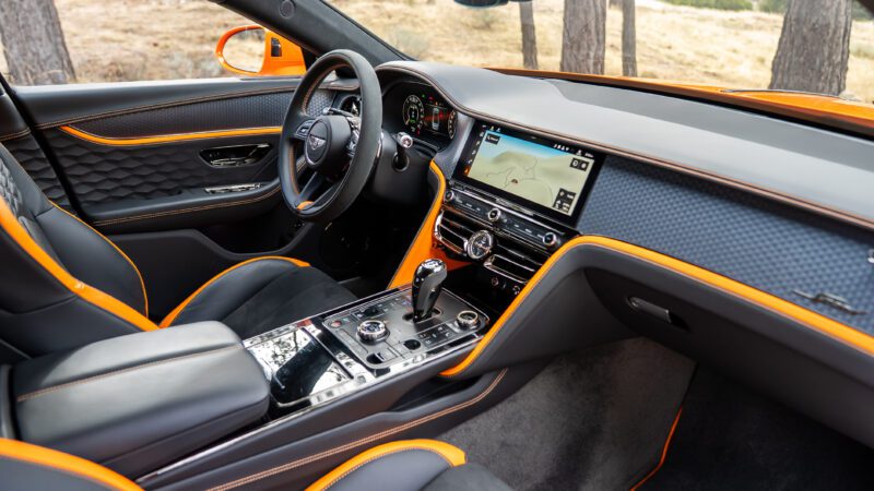 The interior of a luxury car with black leather seats, orange accents, a digital dashboard, touchscreen display with navigation, and various controls on the center console.