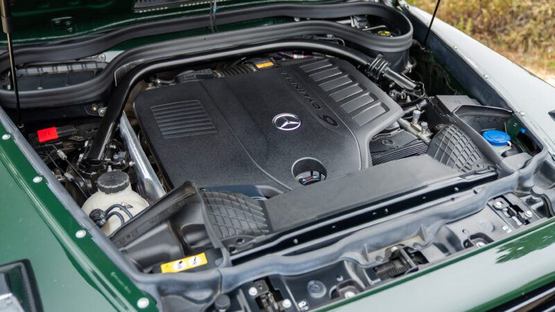 A Mercedes-Benz engine bay showing a clean, modern engine cover with the Mercedes logo and AMG branding, surrounded by various engine components.