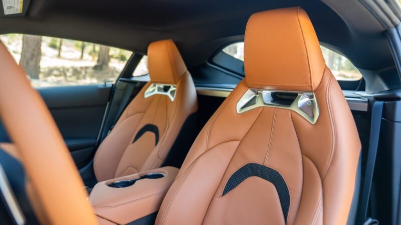 Two tan leather car seats with metal accents and black inserts inside a modern vehicle, shown from the passenger side.