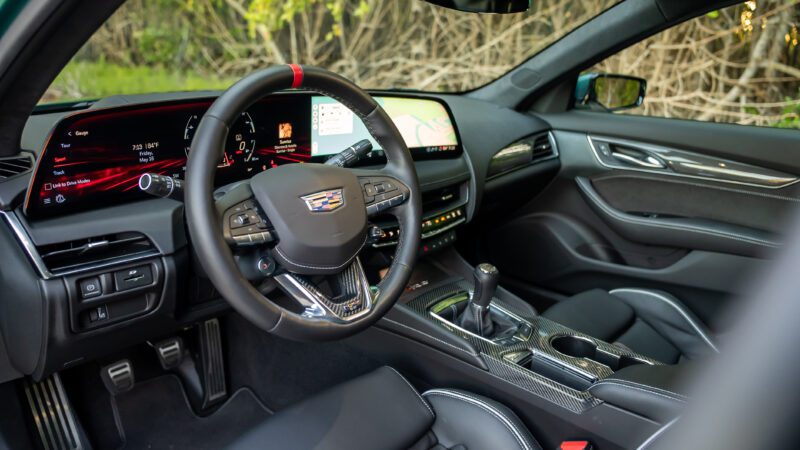 Interior of a modern Cadillac car featuring a digital dashboard, touchscreen display, multifunction steering wheel, manual gear shift, and black leather seats.