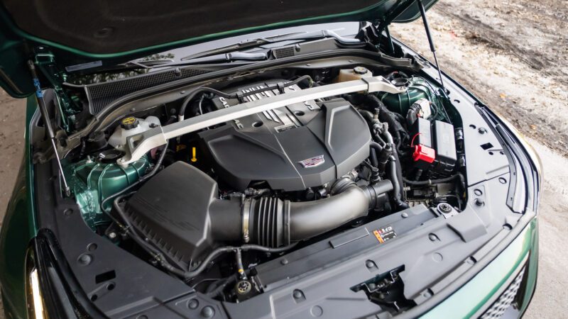 A Cadillac car engine is shown with the hood open, displaying various engine components, air intake system, and battery.