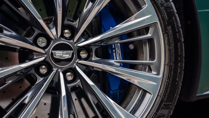 Close-up of a Cadillac car wheel with polished alloy spokes, visible brake disc, and blue performance brake caliper behind it.