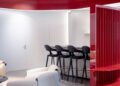 Modern interior with a red ceiling, white walls, black bar stools at a counter, and a curved red room divider next to white armchairs on a patterned rug, reflecting Ferrari’s bold aesthetic and dealer corporate identity.