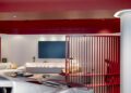 Modern interior space with red ceiling and divider, white walls, a sofa, a TV screen, and part of a Ferrari visible in the foreground—showcasing dealer corporate identity.