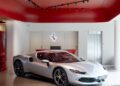 A silver Ferrari sports car is displayed in a showroom with red ceiling panels and modern lighting, reflecting the dealer corporate identity.