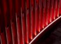 Vertical red slats, inspired by Ferrari’s Dealer Corporate Identity, are evenly spaced with dramatic lighting that casts shadows and highlights, creating an abstract geometric pattern.