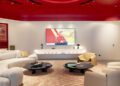 Modern living room with curved white sofas, a beige rug, two round coffee tables, and a large TV on a white wall; red ceiling with circular design and recessed lighting creates a sleek Ferrari-inspired vibe.