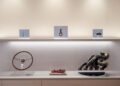 A display shelf featuring a wooden steering wheel, a Ferrari model race car, metal engine parts, and small automotive components under glass covers.