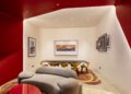 Modern lounge with curved red and white walls, beige sofa, yellow chairs around a black table, and framed Ferrari artwork on the walls—perfect for a stylish dealer showcasing strong corporate identity.