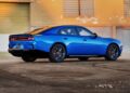 A blue Four-Door Dodge Charger Daytona sedan is parked on a concrete surface in front of a beige industrial building with large windows and a closed green door—but there's more to this muscle car sedan than meets the eye.
