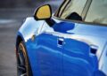 Close-up of the side of a shiny blue Four-Door Dodge Charger Daytona, its yellow side mirror reflecting the sky and surroundings—there’s more to this muscle car sedan than meets the eye.