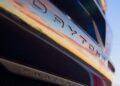 Close-up of a Four-Door Dodge Charger Daytona with its name reflected on the glossy surface and "Fratzonic" on the lower trim, sky colors mirrored in the paint—there's more to this muscle car sedan than meets the eye.