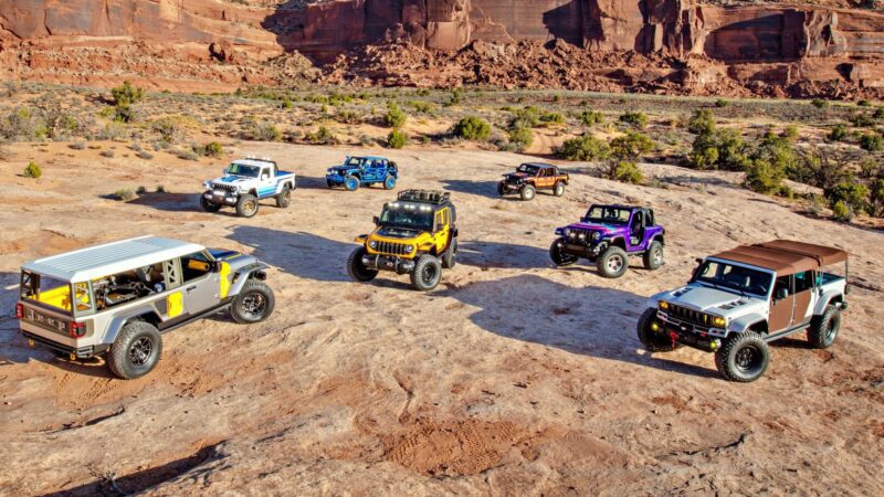 Seven off-road vehicles are parked on rocky terrain in a desert landscape with red cliffs, showcasing one thing that makes this carbon-fiber tent a game changer for the Jeep Wrangler: ultimate durability and comfort for any adventure.