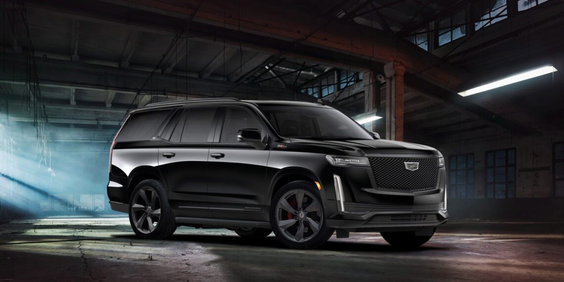 A black Supercharged Escalade SUV is parked inside a dimly lit, industrial warehouse with concrete floors and exposed beams.