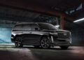 A black Supercharged Escalade SUV is parked inside a dimly lit, industrial warehouse with concrete floors and exposed beams.