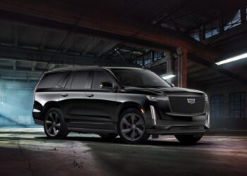 A black Supercharged Escalade SUV is parked inside a dimly lit, industrial warehouse with concrete floors and exposed beams.