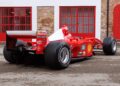 Red Formula 1 car with visible sponsor logos, parked on wet pavement before red garage doors and a brick wall—this is the iconic Ferrari F2001 from the Historic Monaco Sale, where it became the most valuable Schumacher-F1 car auctioned at €15.98 million.